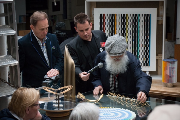Yaacov Agam demonstrates his Beating Heart sculpture to Park West VIP guests at a studio visit celebrating his 86th birthday. Park West's Jason Betteridge and founder and CEO Albert Scaglione look on.