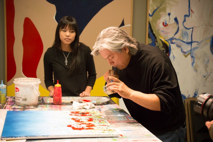 Dominic Pangborn demonstrates for the TV crew and a student a primitive airbrush technique using a straw.