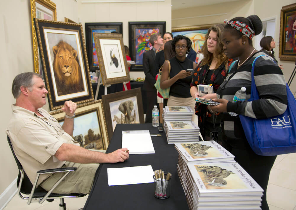 Andrew Bone singing copies of his book "Brush Strokes of Africa," which collects examples of his breathtaking art and his memories of growing up in Zimbabwe.