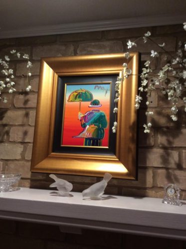 a Peter Max painting hung above a fireplace in a gold frame