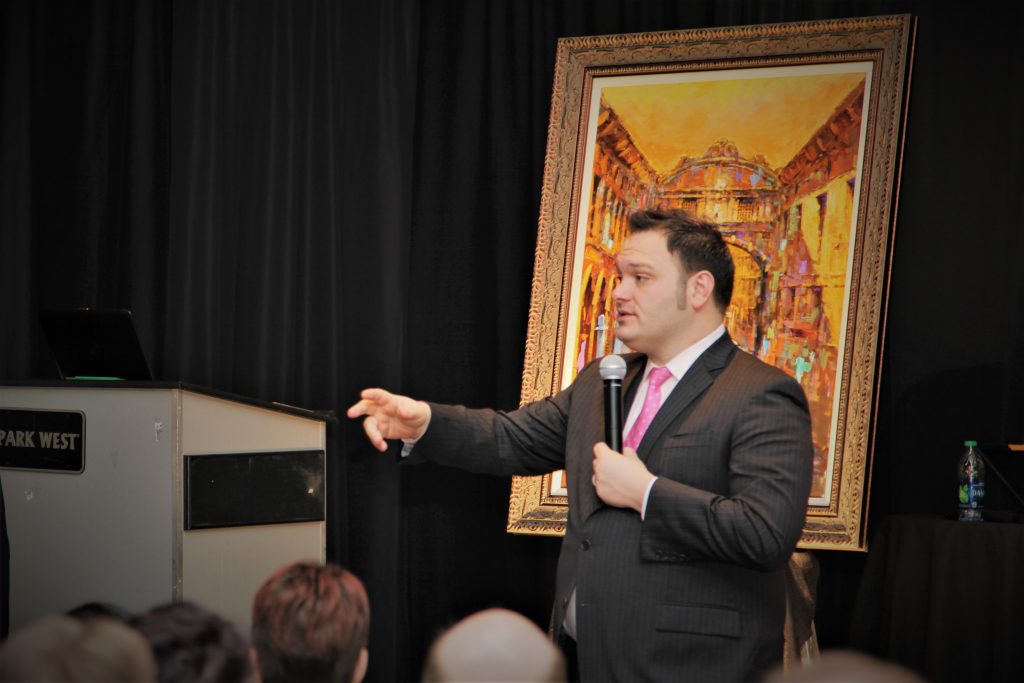 Art auctioneer standing in front of a large framed painting that he is selling