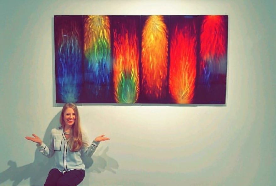 girl sits in front of a large metallic painting hanging on an art gallery wall