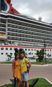 Nikki and her partner pose in front of one of the cruise ships where she works as an auctioneer.